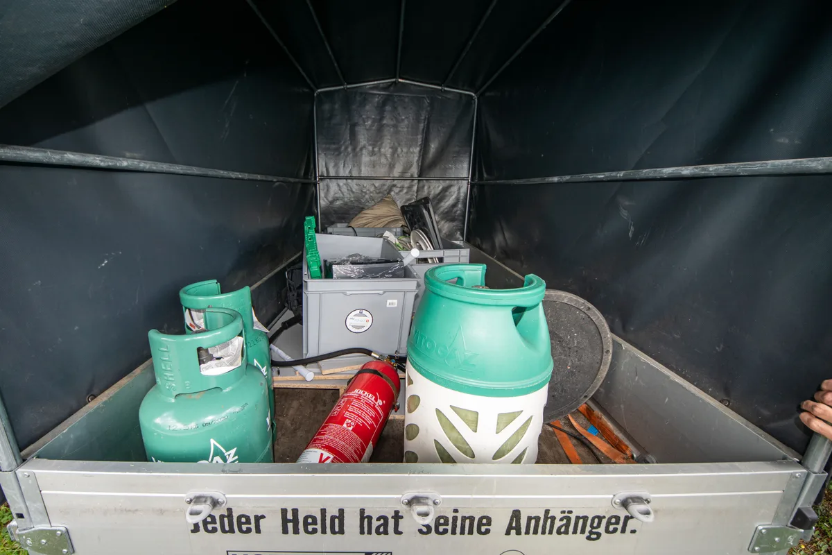 Man sieht Gasflaschen und Plastikboxen in einem Anhänger.